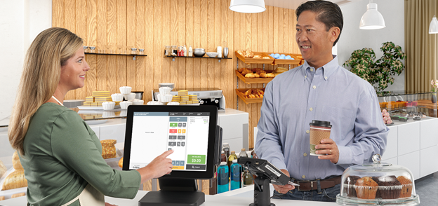 Woman using a point of sale system to check out a man buying coffee